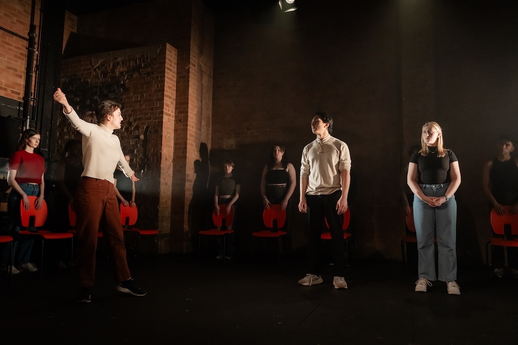 Action shot of the spring 2024 Shakespeare in Performance at RADA final presentation of Julius Caesar. Three actors stand in mid-performance as others are behind them, looking on.